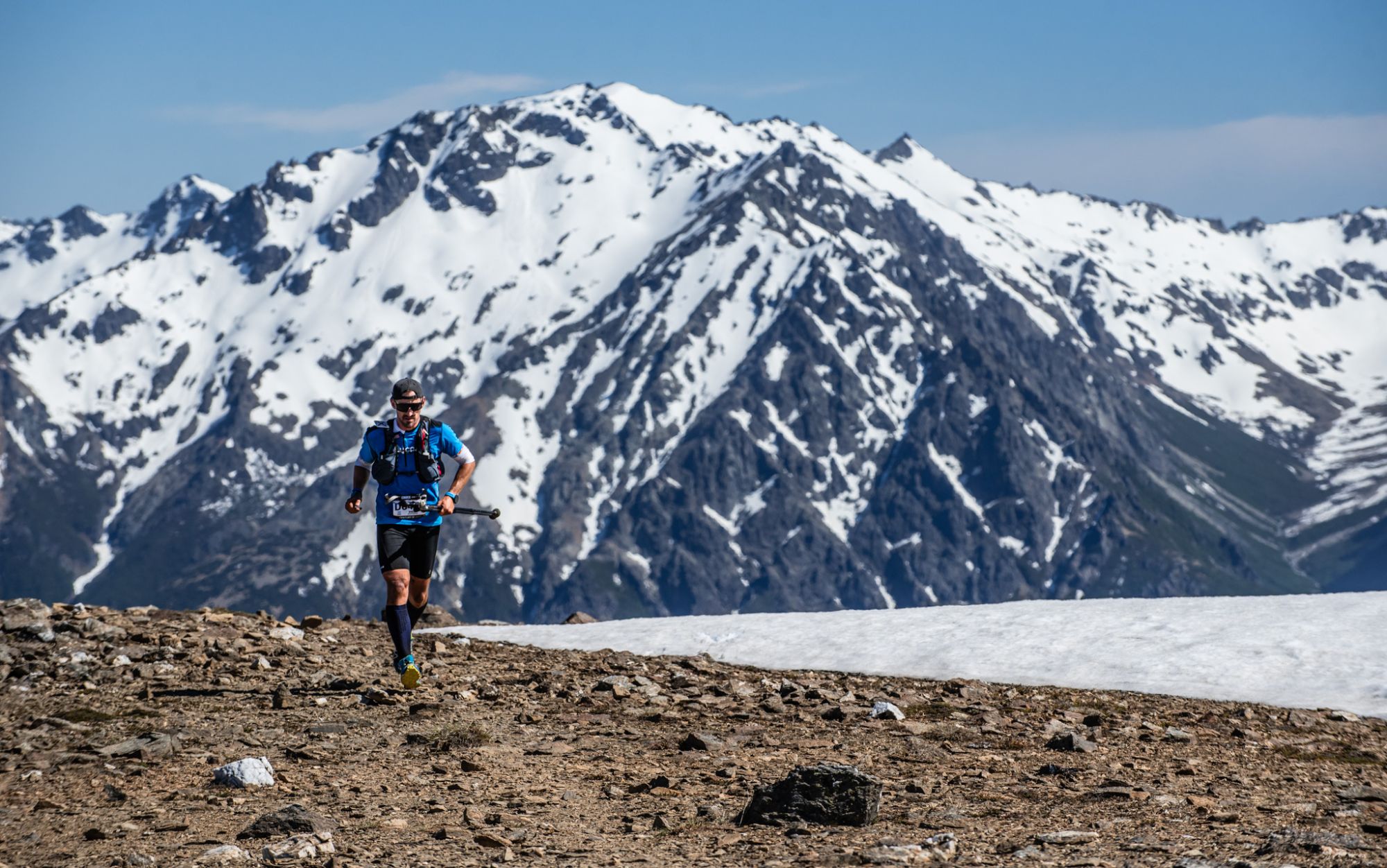 A runner moves along a rocky ridge facing the snowy range