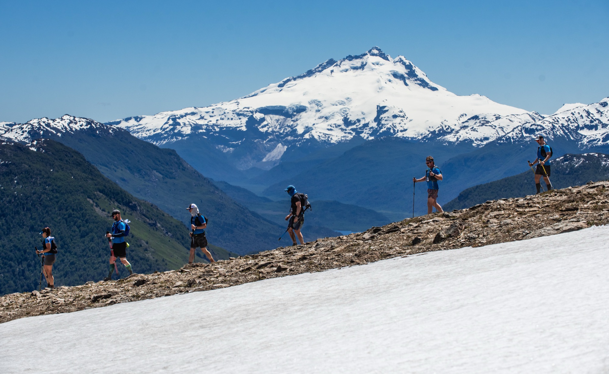 Corredores en fila sobre un filo, con el cerro Tronador nevado detrás