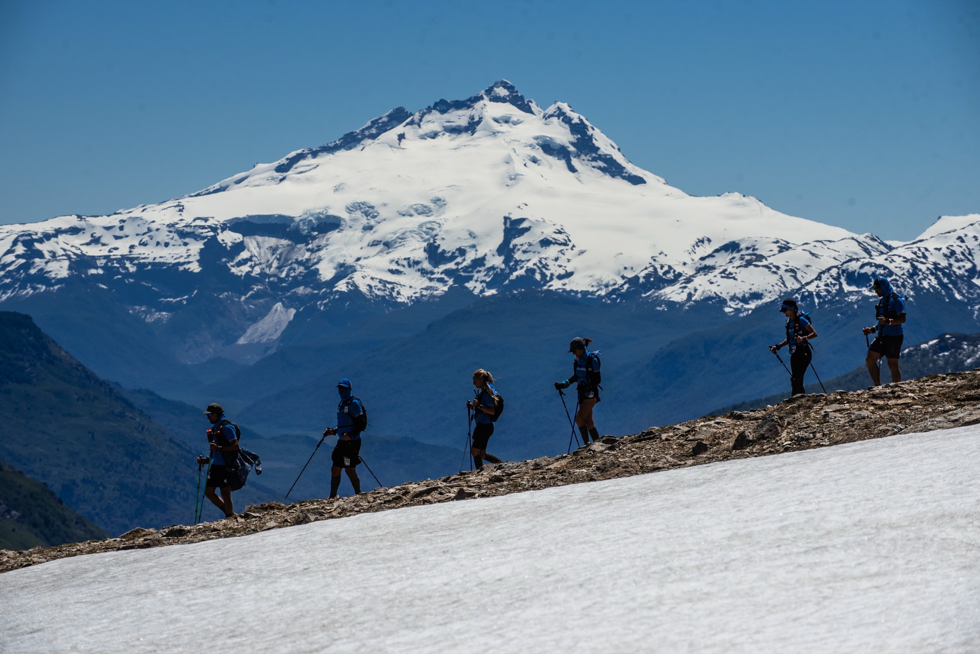Corredores en fila sobre un filo nevado, con el cerro Tronador de fondo