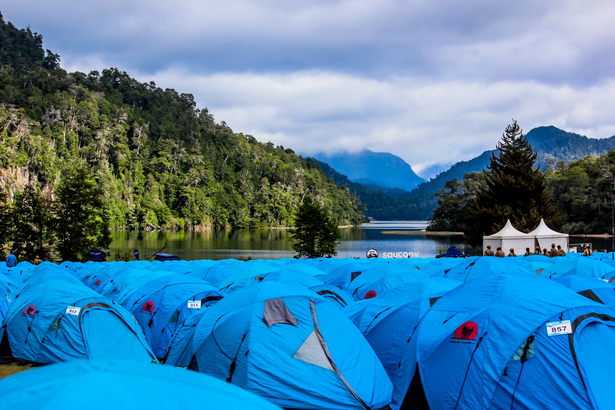 Blue camp tents on the lakeshore, with the mountains in the background