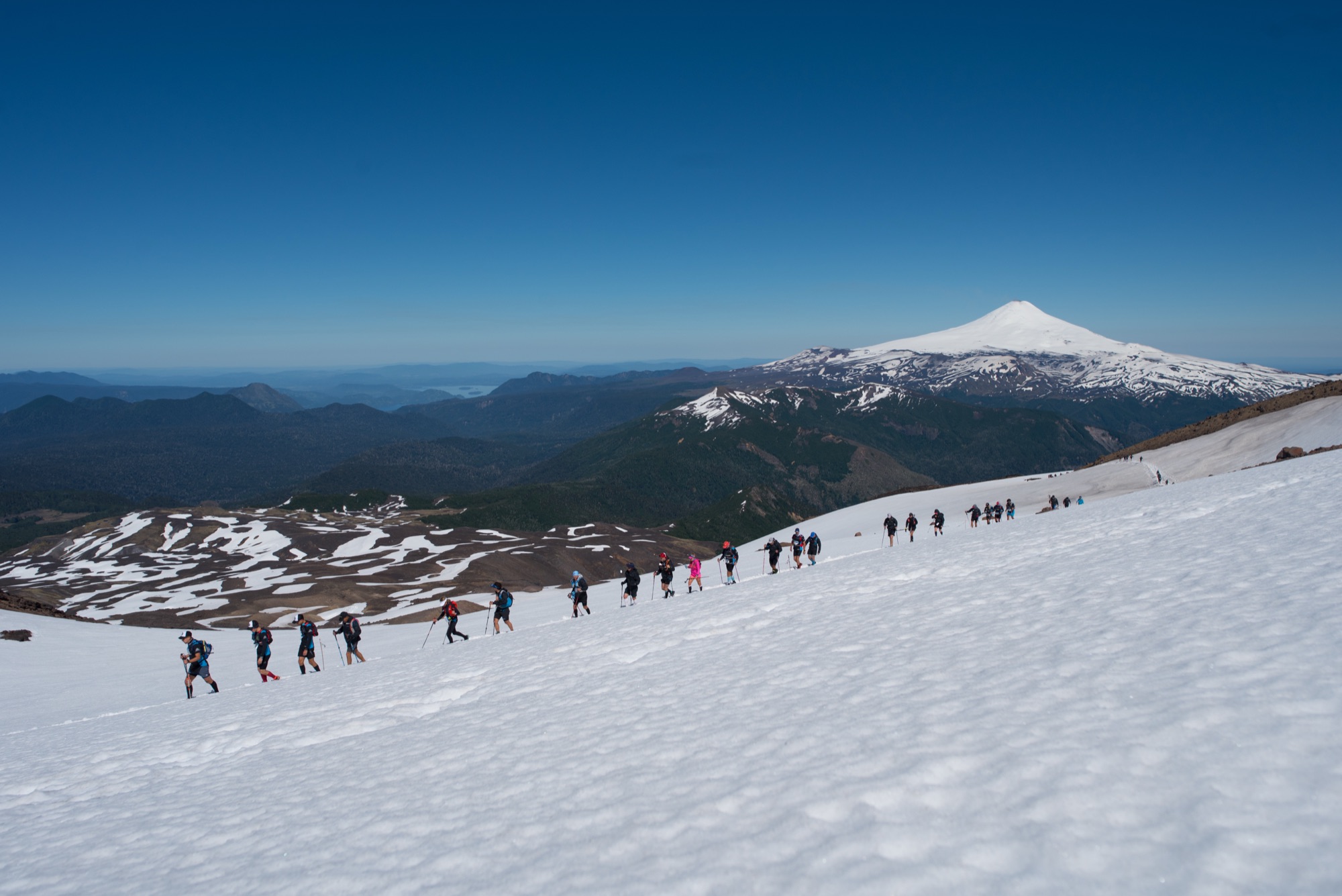 Runners crossing a snowfield with a volcano in the background