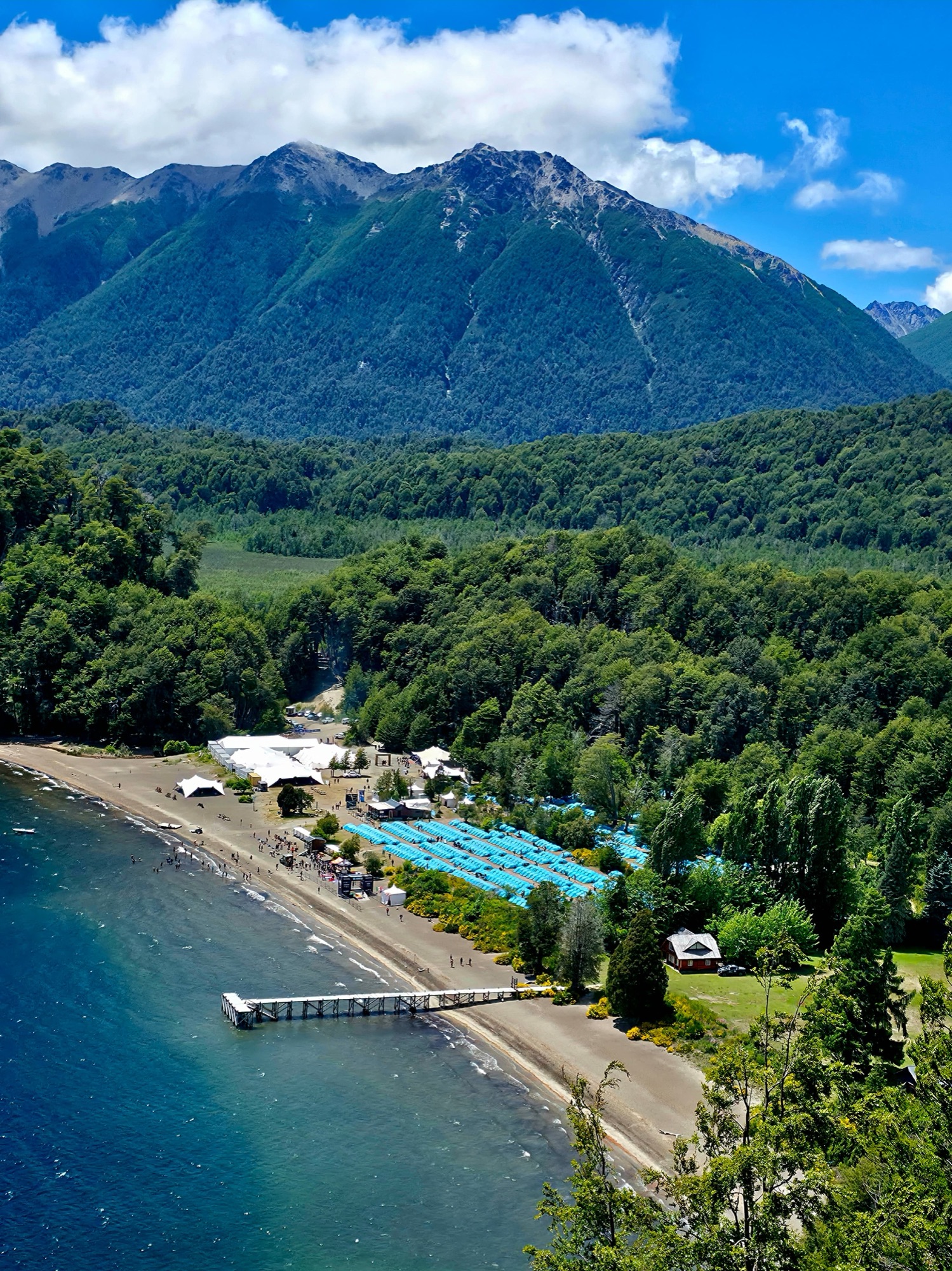 Aerial view of a camp on the shore of a lake, between forest and mountains