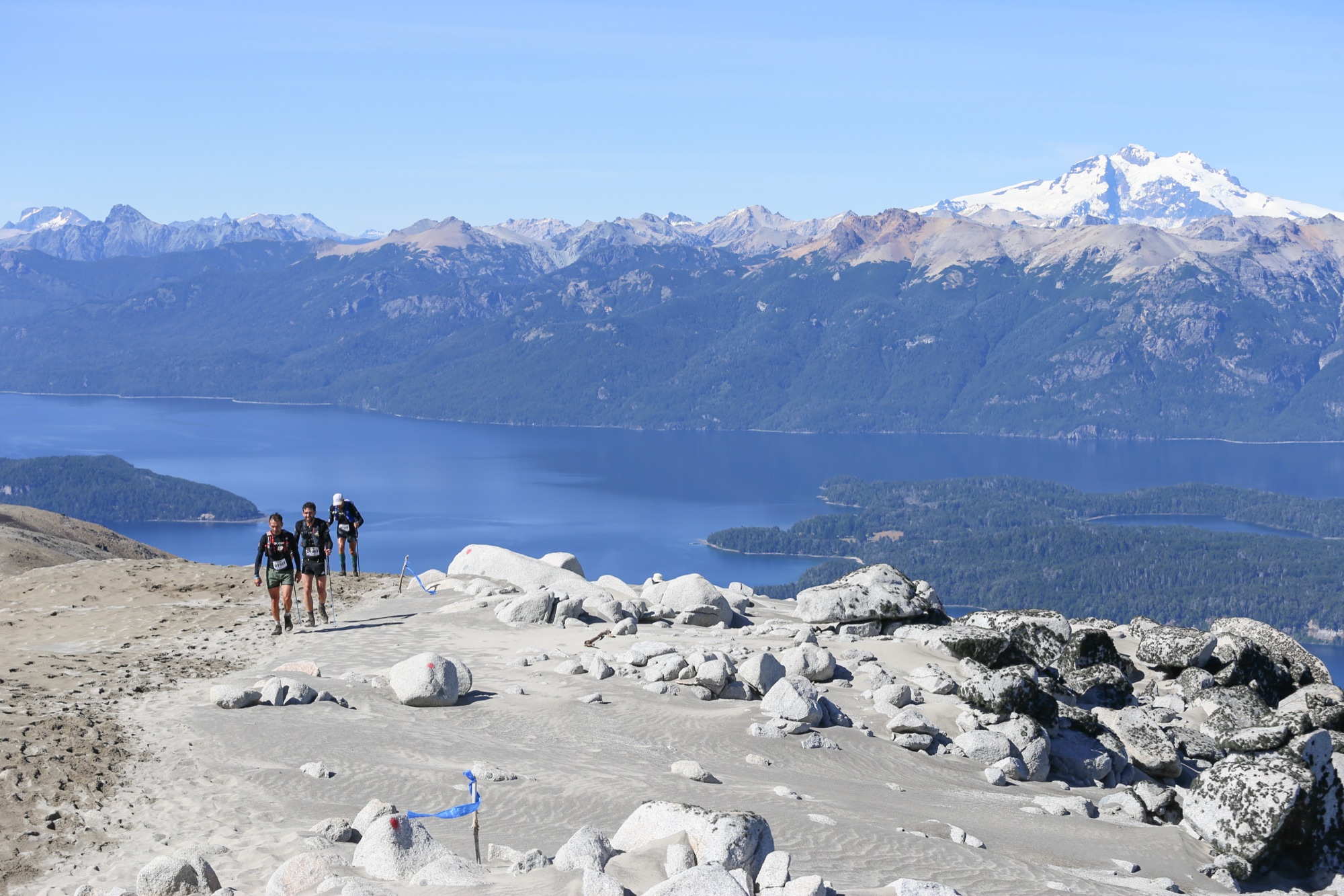 Corredores en una cumbre con el lago y la cordillera nevada de fondo