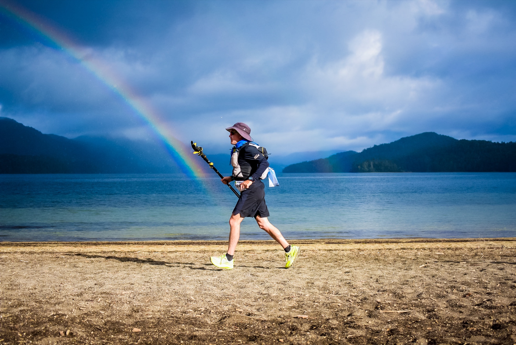 A runner moves along the lake beach with a rainbow behind